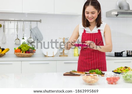 Asian housewife proudly takes a picture of her homemade food with her phone.
