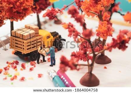 Top view miniature toy figurines of alone courier man delivering a box  in autumn, fall season or during cherry blossom season concept -  warm tone filter applied.
