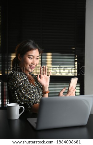 Portrait of a smiling young woman making video call with smart phone at modern office.