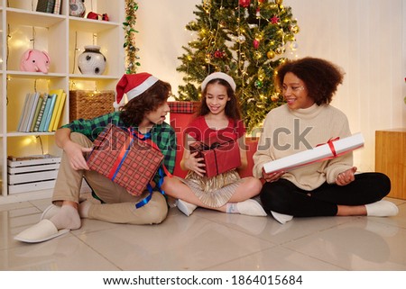 Group of excited kids opening their Christmas presents when sitting under decorated tree at home