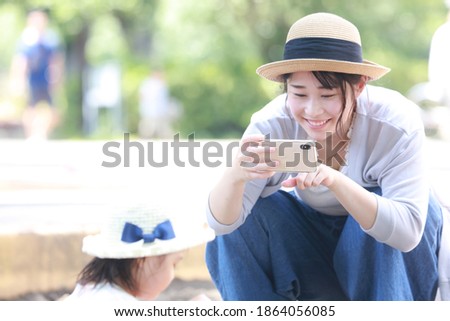 A mother taking a picture of a child playing in the sandbox with a smartphone