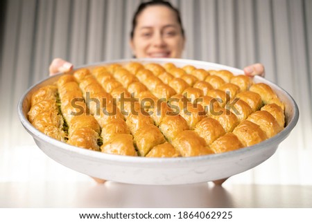 She lifts the tray of baklava dessert in her hand and smiles at the camera deep in the field Royalty-Free Stock Photo #1864062925
