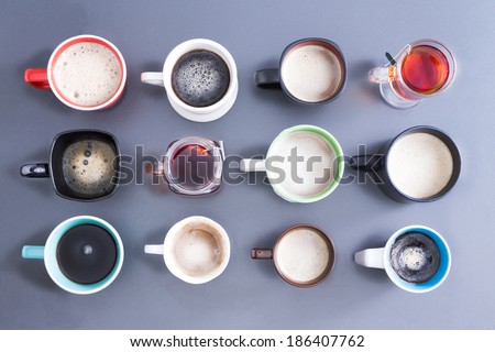 Conceptual image depicting the Time for your daily dose of caffeine with an overhead view of a neat arrangement of twelve different cups, mugs and glasses filled with hot fresh tea and coffee on grey