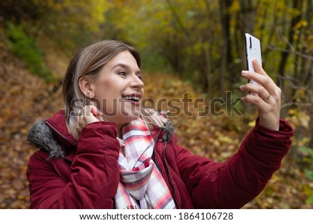 Beautiful young woman making online content with smartphone, colorful autumn background