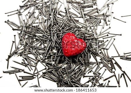 Red love heart on pile of iron nails