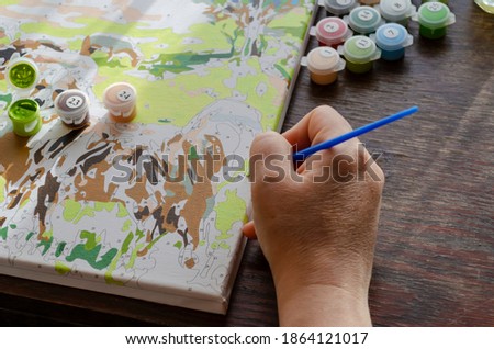 Active leisure at home, creative hobby concept. Hands of an adult woman painted with brush picture of numbers. Numbered paints. Drawing by numbers.