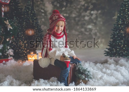 Littlw toddler child with suitcase and little gingerman toy in hand, walking in a snowy forest, christmas theme picture