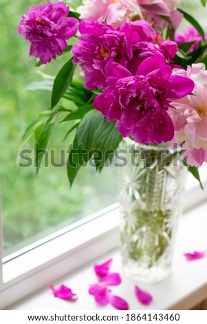 Vertical photo of vase with bright peonies bouquet. Windowsill with flower bunch