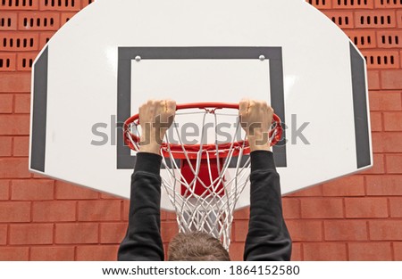 Man hanging on basket in a school gym, red brick wall