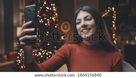 Happy girl videocalling her friends from home and taking selfies with her smartphone on Christmas day