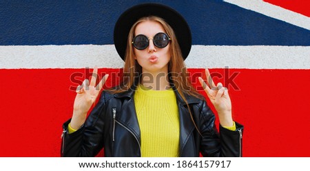 Portrait of beautiful young woman model blowing lips wearing a black round hat, jacket in the city