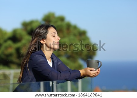 Relaxed woman with closed eyes holding coffee mug in a hotel balcony on the beach Royalty-Free Stock Photo #1864169041