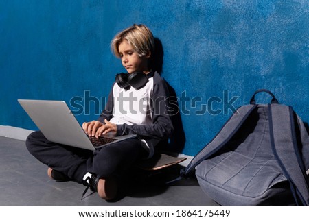 Clever teen boy typing on laptop studying preparing for test exam doing homework, school exercises, sitting on skateboard with backpack. Schoolboy learning assignment. Teen education concept.