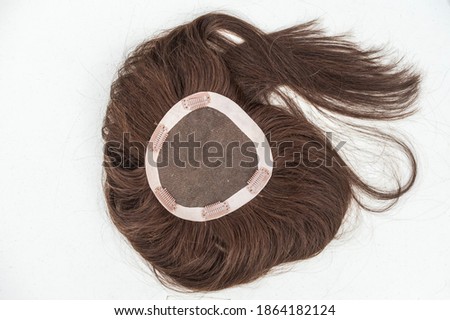 View of the inside of a brunette toupee or hair topper showing the clips against a plain white backdrop. Royalty-Free Stock Photo #1864182124