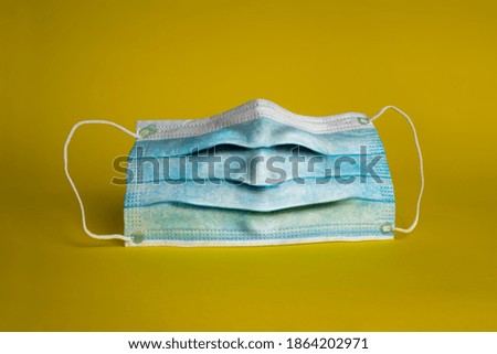 funny surgical mask with a face in a happy expression with the rubber bands as ears. Protective face mask on a yellow background