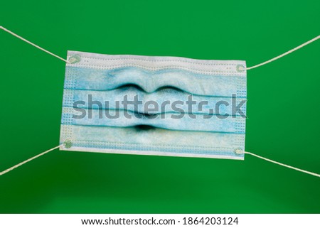 funny surgical mask with a stressed expression face with stretched rubber bands. Protective mask on a green background