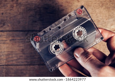 Hand holding audio cassette tape on brown old wooden table. Minimalism retro style concept. Background pattern for design. 
