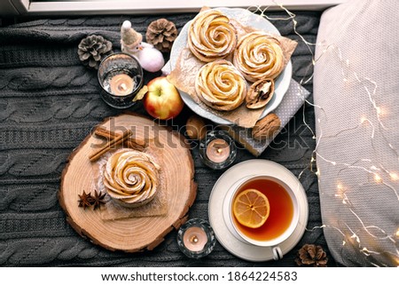 A cup of hot tea with lemon in an early winter morning by the window. Knitted wool warm blanket, hot homemade apple cakes with cinnamon and star anise . Decor. Home winter holiday concept.