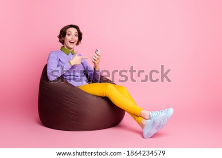 Full size profile side photo of surprised girl sit bean chair point finger smartphone isolated pastel color background
