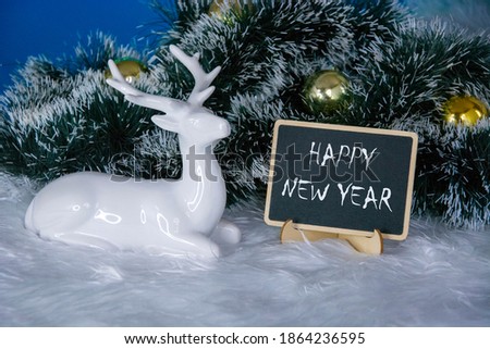 Deer on Christmas background. A spruce branch with Golden Christmas balls and the inscription Happy New year written in chalk on the Board.