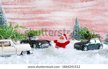 Toy Santa in the forest among the snowdrifts, waves to cars that are delivers Christmas trees. Magic atmosphere, concept of Christmas holidays. Greeting card.