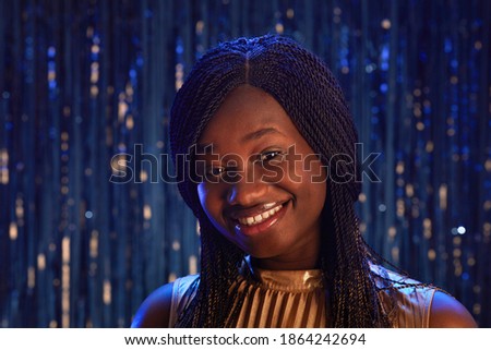 Portrait of smiling African-American girl looking at camera while standing against sparkling background at party, copy space
