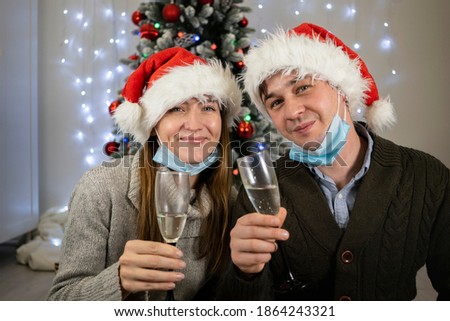 Happy married couple in protective masks drinks champagne for christmas. Family new year during quarantine covid 19 pandemic safe at home