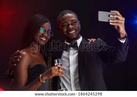 Waist up portrait of elegant African-American couple taking selfie photo while enjoying party