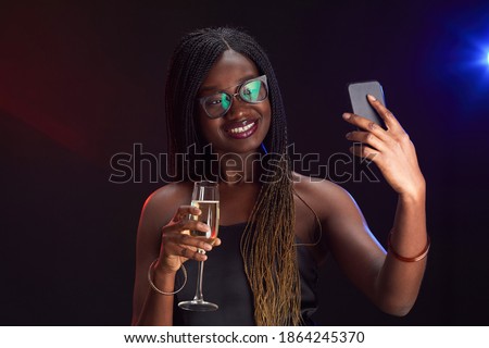 Portrait of elegant African-American woman holding champagne glass and taking selfie photo while enjoying party, copy space