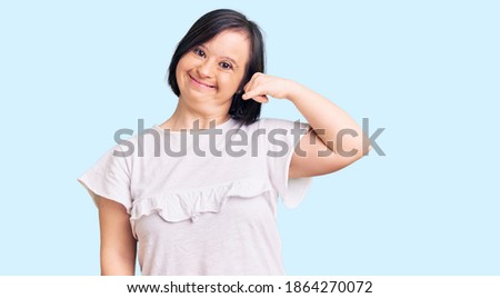 Brunette woman with down syndrome wearing casual white tshirt smiling doing phone gesture with hand and fingers like talking on the telephone. communicating concepts. 