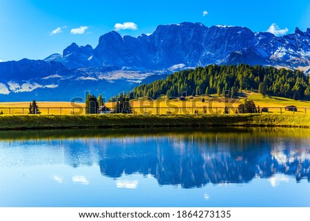 Alpe di Siusi picturesque plateau in the Dolomites. Beautiful sunny summer day. In small pond sky and mountains are reflected. The concept of walking, ecological and photo tourism