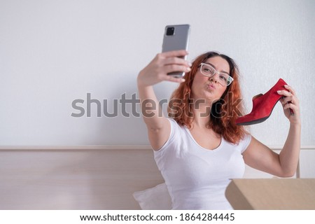 Caucasian woman sitting in bed and taking a selfie with a delivered purchase. Online shopping for shoes