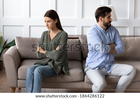 Stubborn angry man and woman spouses sit separate on sofa at home ignore each other avoid talking after fight. Unhappy mad young Caucasian couple think of divorce breakup after family fight quarrel. Royalty-Free Stock Photo #1864286122