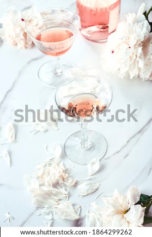 Rose wine in glasses and beautiful white peonies and a scattering of petals on a white marble background. Romantic dinner concept, Saint Valentine's day