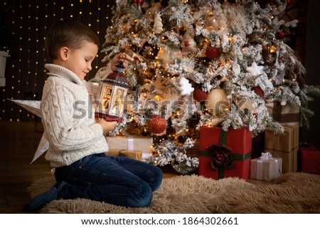Little boy in holding a white lantern in his hand and sitting near the Christmas tree at home, Happy New year