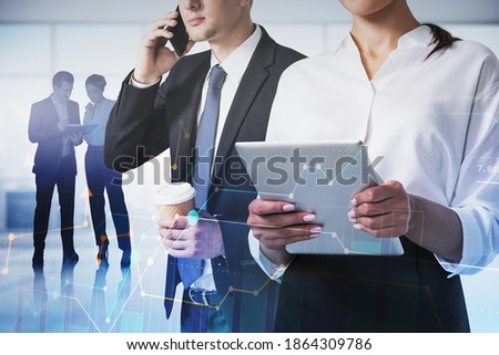 Businessman on phone and businesswoman with tablet in blurry office with their colleagues in background and double exposure of graphs. Toned image