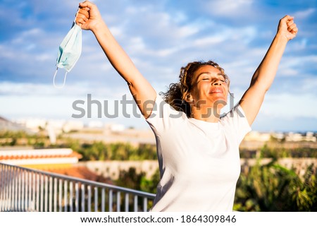 one happy curly woman outdoors in her balcon of her home without medical mask with opened arms looking at the sky after quarentine and after passed the coronavirus or covid-19 - no more mask  Royalty-Free Stock Photo #1864309846