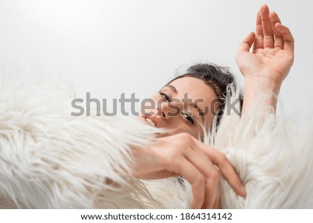 top view of elegant brunette young woman in stylish faux fur jacket posing on white background