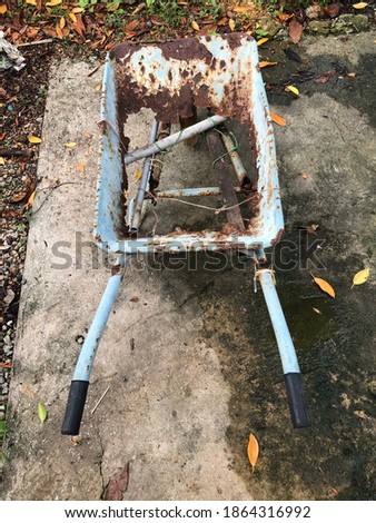 An old, broken, rusty trolley or wheelbarrow on lawn. Wheelbarrow is damaged, cannot be used. Out of focus, noise and grain effects.