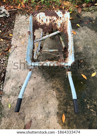 An old, broken, rusty trolley or wheelbarrow on lawn. Wheelbarrow is damaged, cannot be used, out of focus, noise amd grain effects.