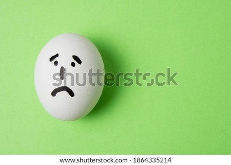 Egg with a very sad emotion on the face, on a green background with copy space