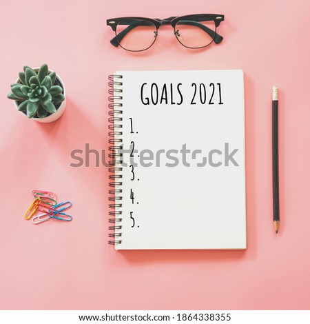 2021 New year concept. Goals list in notepad, smartphone, stationery on pink pastel color with copy space