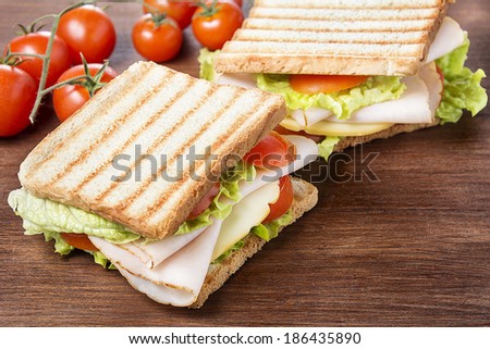 Sandwiches with chicken breast, salad, cheese and tomatoes on wooden table