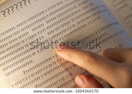 A person leads a finger on the lines in the book, but instead of letters only question marks on the page in the textbook. Royalty-Free Stock Photo #1864366570
