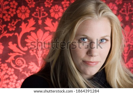 Studio portrait of a young woman with long blonde hair looking at camera. Isolated on red patterned background.