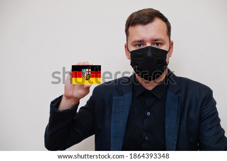 German man wear black formal and protect face mask, hold Saarland flag card isolated on white background. Germany states coronavirus Covid concept.
