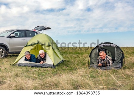 Elderly male tourists friends i are resting in a tent against the backdrop of a cloudy sky on a summer day.