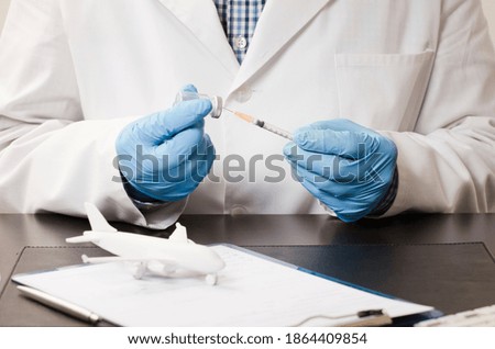 Doctor with blue gloves and syringe and vaccine, office table with white plane, pen, computer keyboard, white background