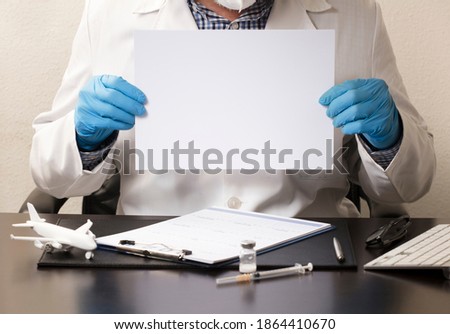 Doctor with blue gloves, white poster in hands (to fill out), desk with syringe, vaccine, airplane, glasses, white form and computer keyboard