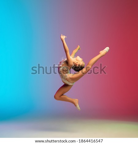 High jump. Little caucasian girl, rhytmic gymnast training, performing isolated on gradient blue-red studio background in neon. Graceful and flexible, strong child. Concept of sport, motion, action.